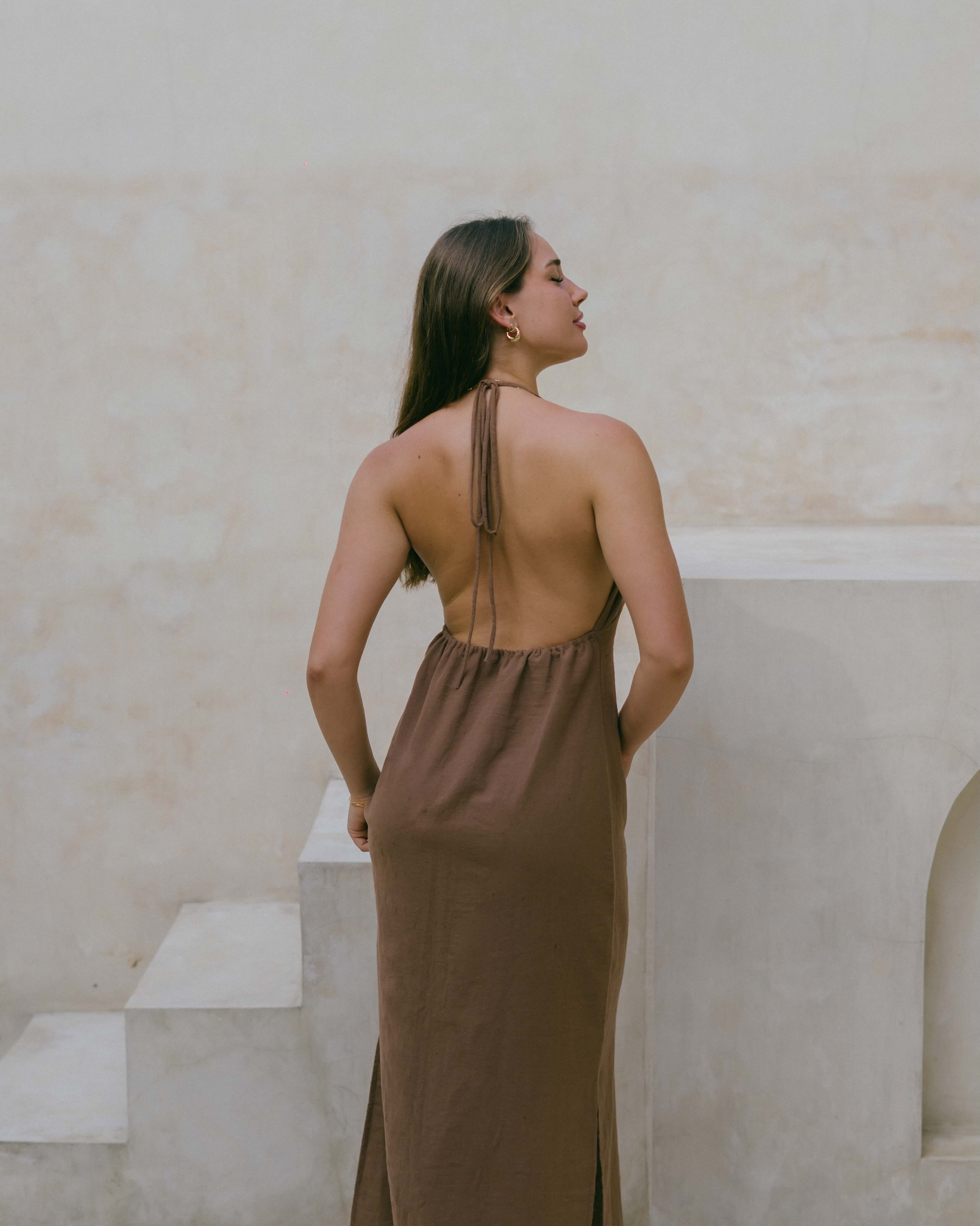 Flattering and versatile, the Palma Halter Maxi Dress features an open back, ruched bust, and relaxed fit for chic summer wear.