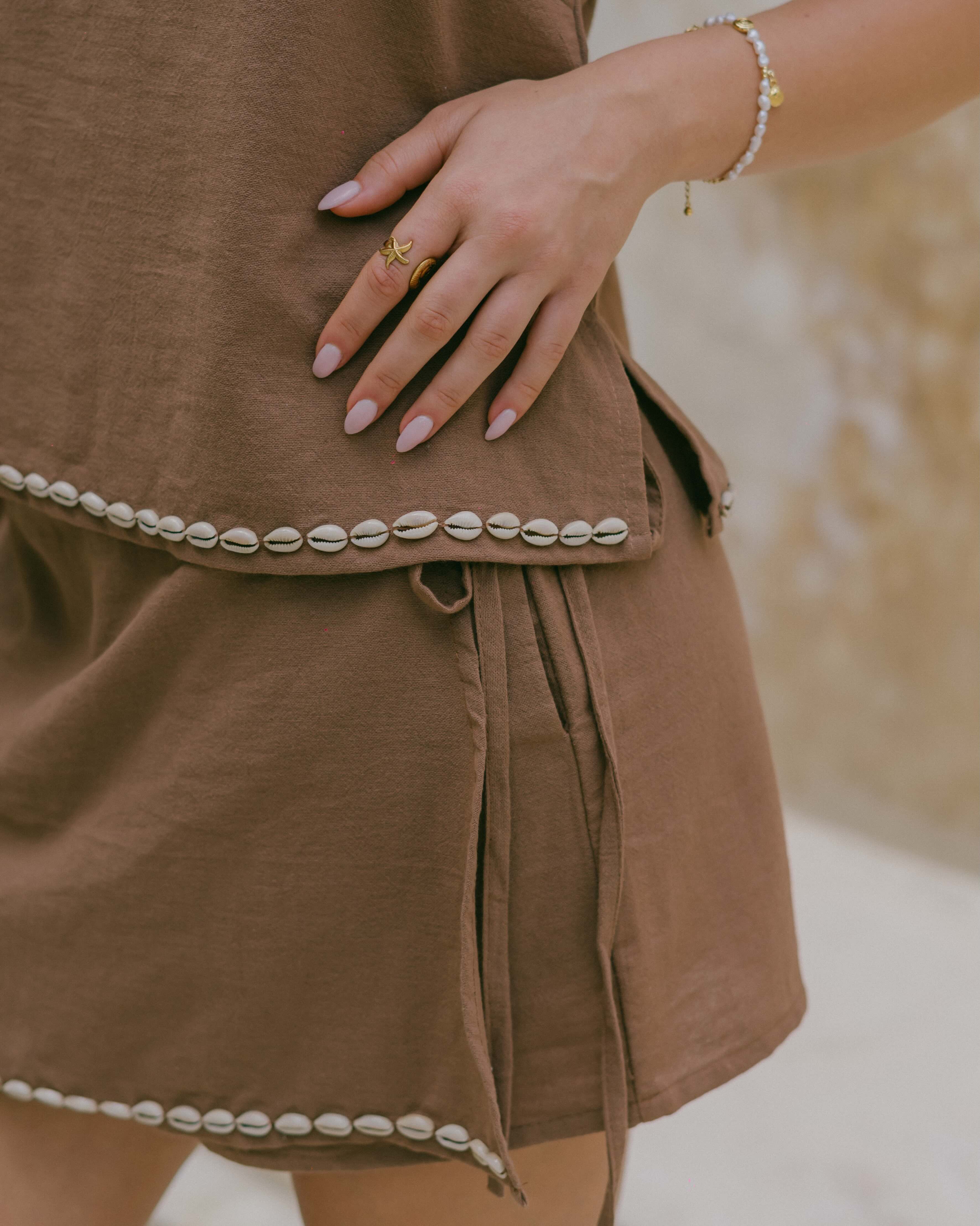 Designed for sun-filled days, the Coralie Shell Skort offers breezy comfort with functional pockets, a wrap front, and ocean-inspired shell accents.