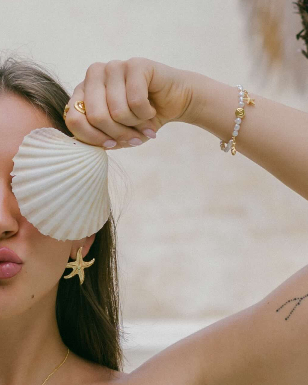 Shop the golden days Pearl Bracelet—freshwater pearls with three gold charms: a starfish, swirl, and scallop shell. A delicate coastal-inspired accessory.