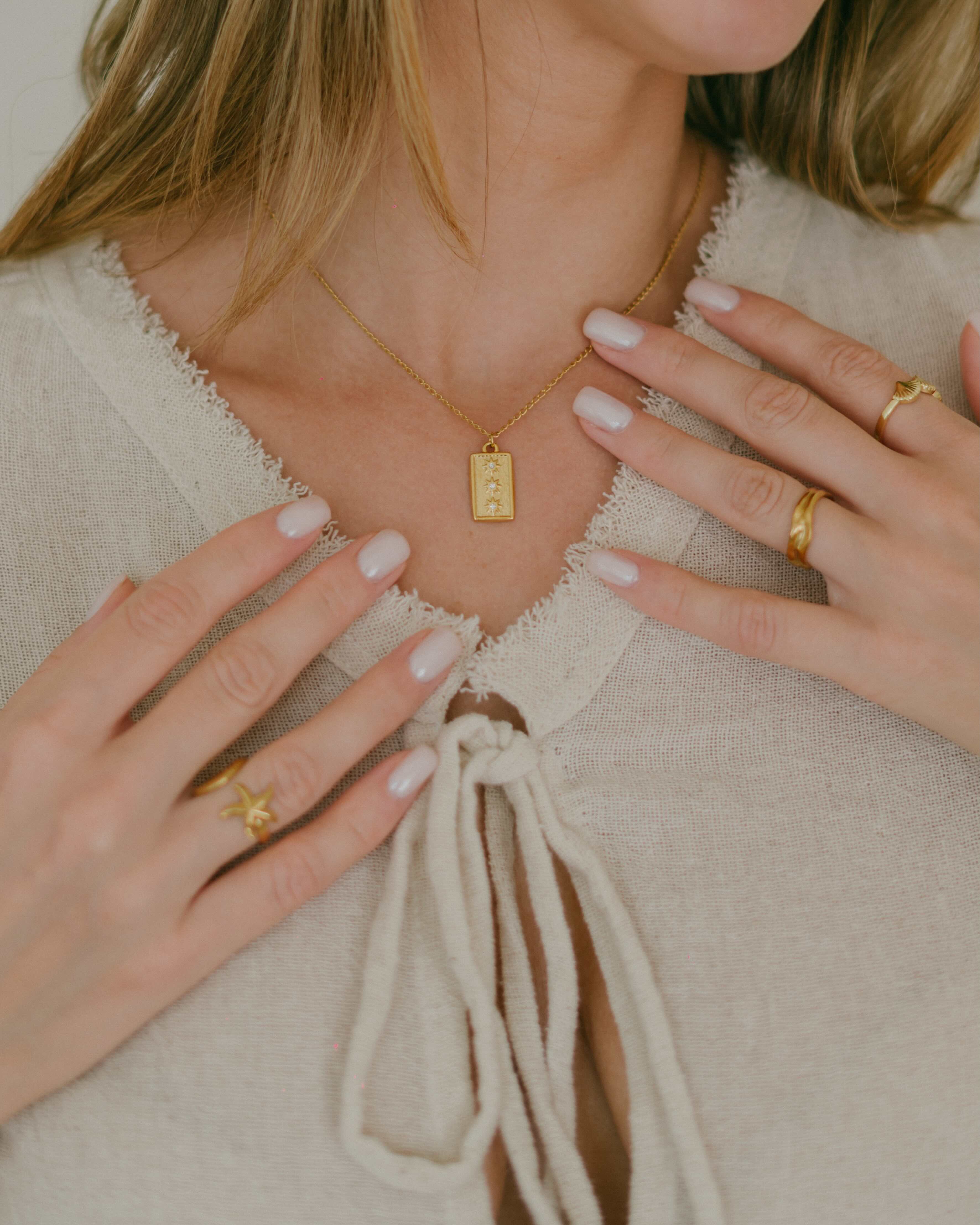 Shop the Junie Necklace—an 18k gold plated waterproof necklace with a vertical rectangle pendant featuring three sun designs, each set with a sparkling gemstone. Perfect for layering or statement wear.