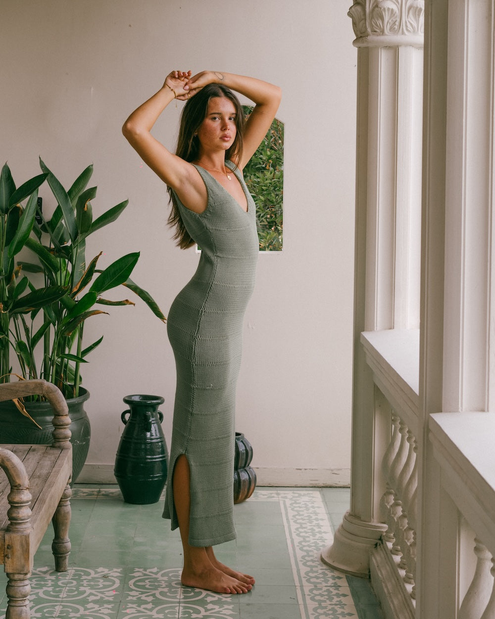 Noa Knit Dress in Sage, sleeveless ribbed knit maxi dress with V-neck, styled among indoor plants and an arched mirror
