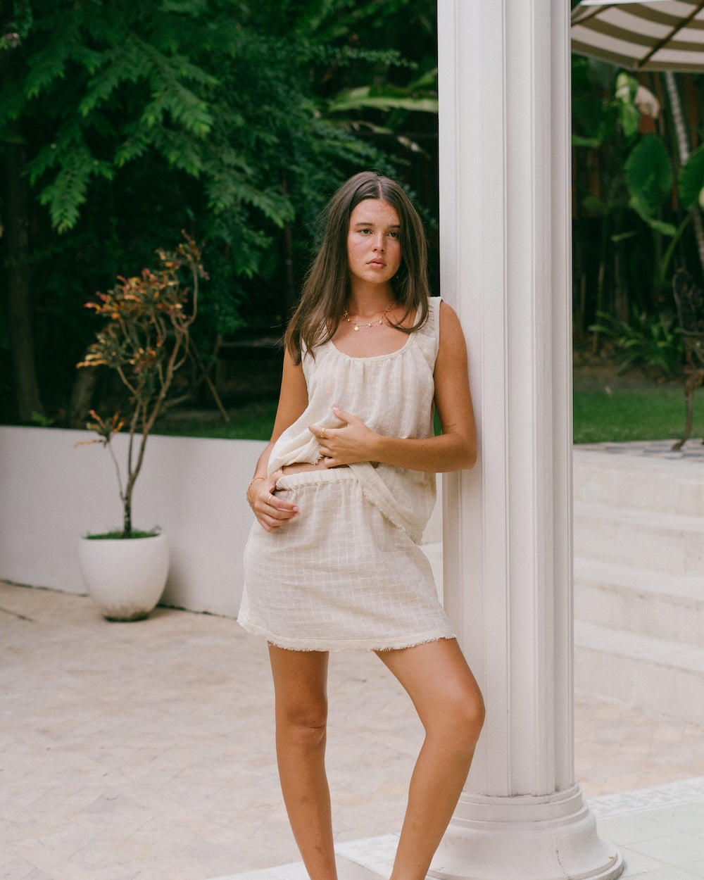 Sofia Singlet Top and Mini Skirt styled as matching set — model leaning against white column, front full-length view showing gathered neckline, frayed hem singlet and mini skirt with elasticated waistband — check ramie co-ord set — Malia The Label Australia