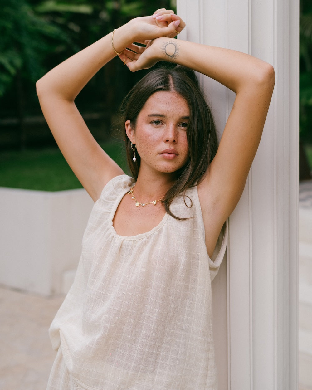 Sofia Singlet Top close portrait — model leaning against white column with arms raised, gathered rounded neckline and checked ramie fabric texture clearly visible, gold jewellery styling — natural ramie singlet top — Malia The Label La Dolce Vita collection Australia