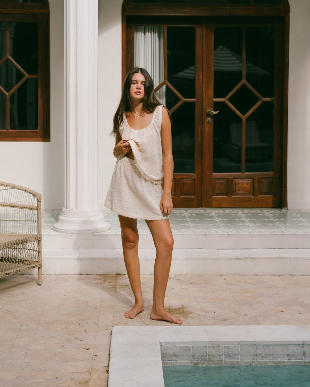 Sofia Singlet and Mini Skirt set poolside — model standing at pool edge, relaxed front-facing full-length shot showing natural check ramie co-ord with frayed hems — breathable summer matching set — Malia The Label slow fashion