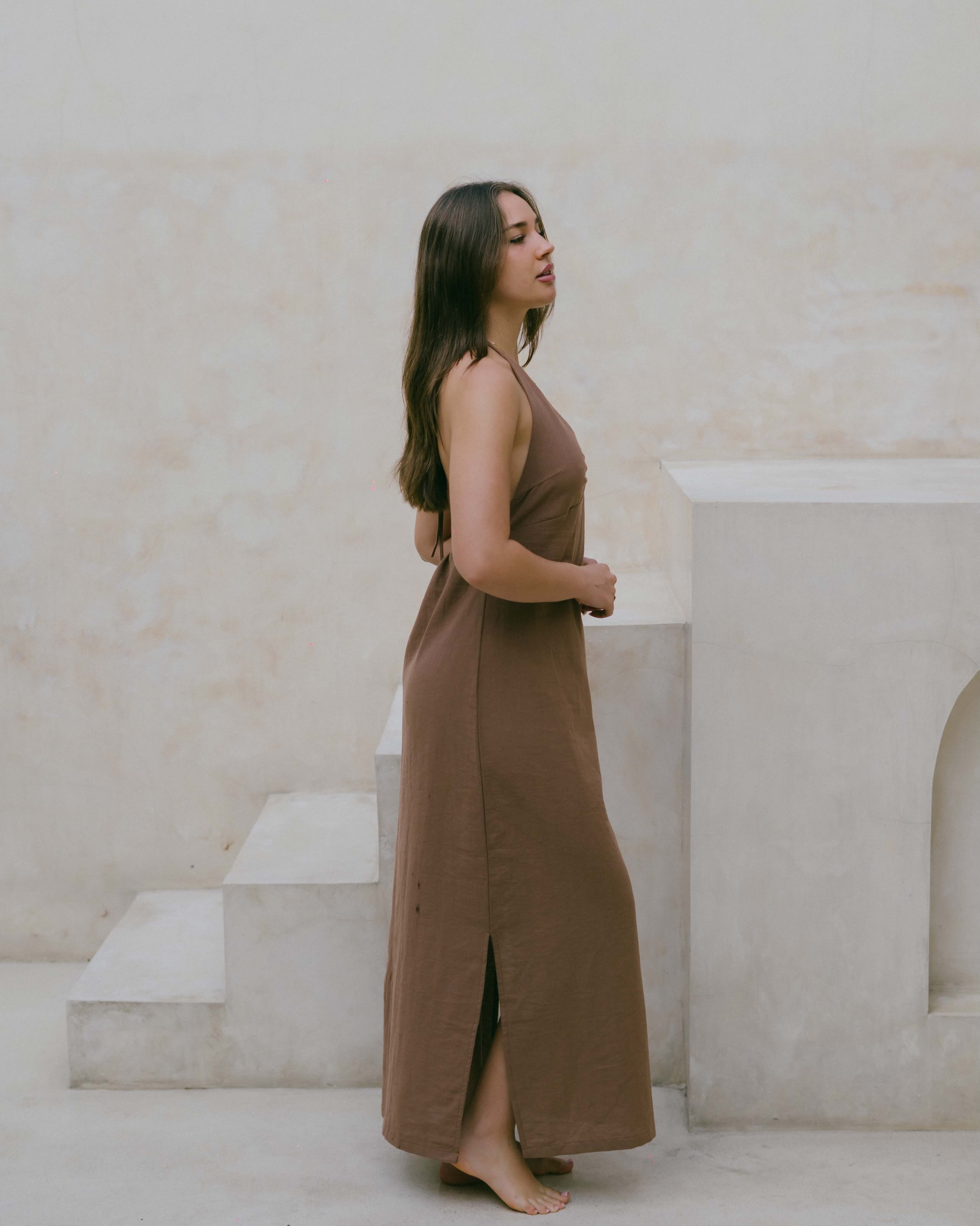 Step into effortless beauty with the Palma Halter Maxi, a chocolate maxi dress with a tie-up neckline, side slits, and timeless design.

