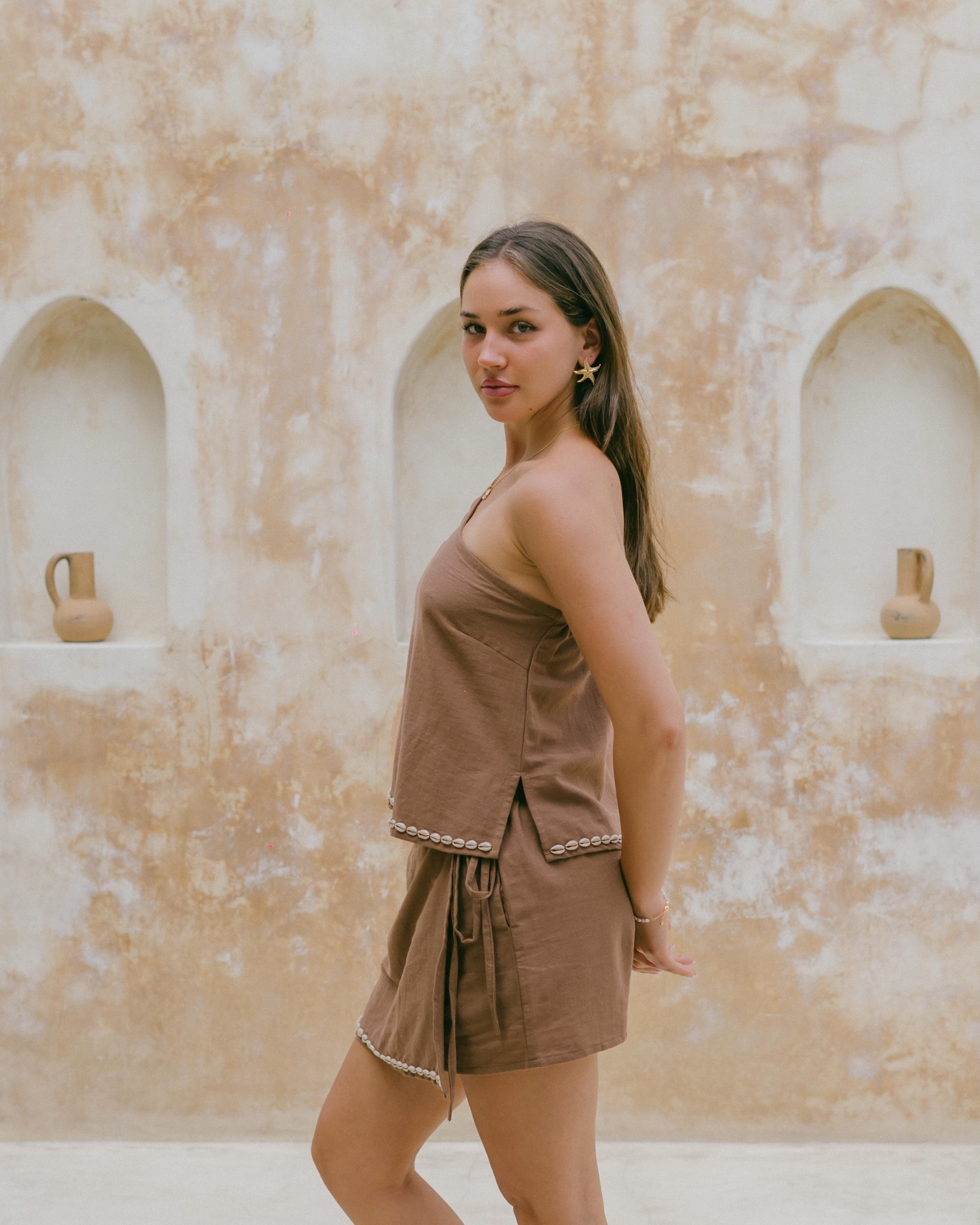 Elevate your summer wardrobe with the Coralie Shell Top, crafted in a rich chocolate hue with a tie-up shoulder and ocean-inspired details.