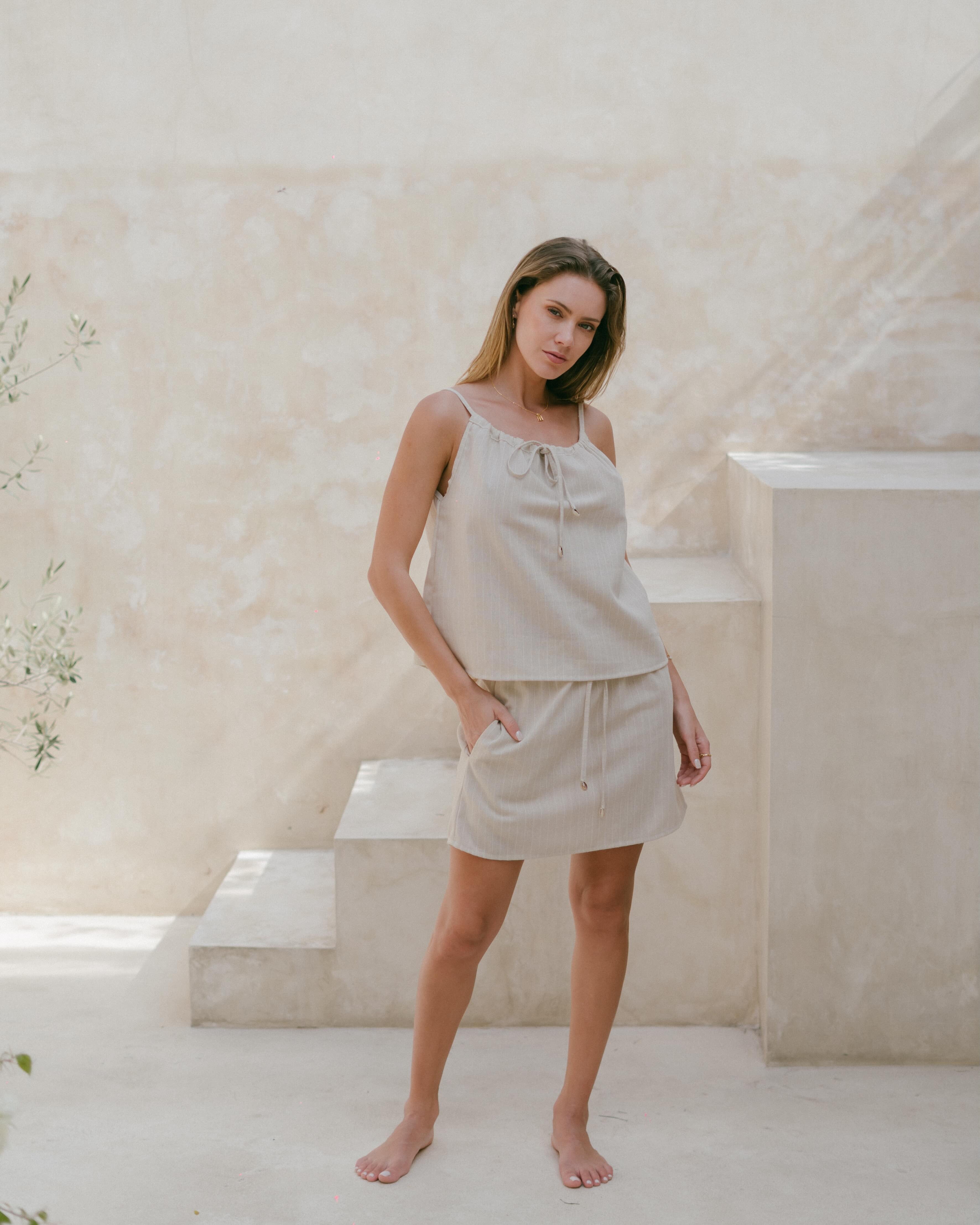 Lightweight neutral pinstripe top with adjustable straps and coastal-inspired shell accents.