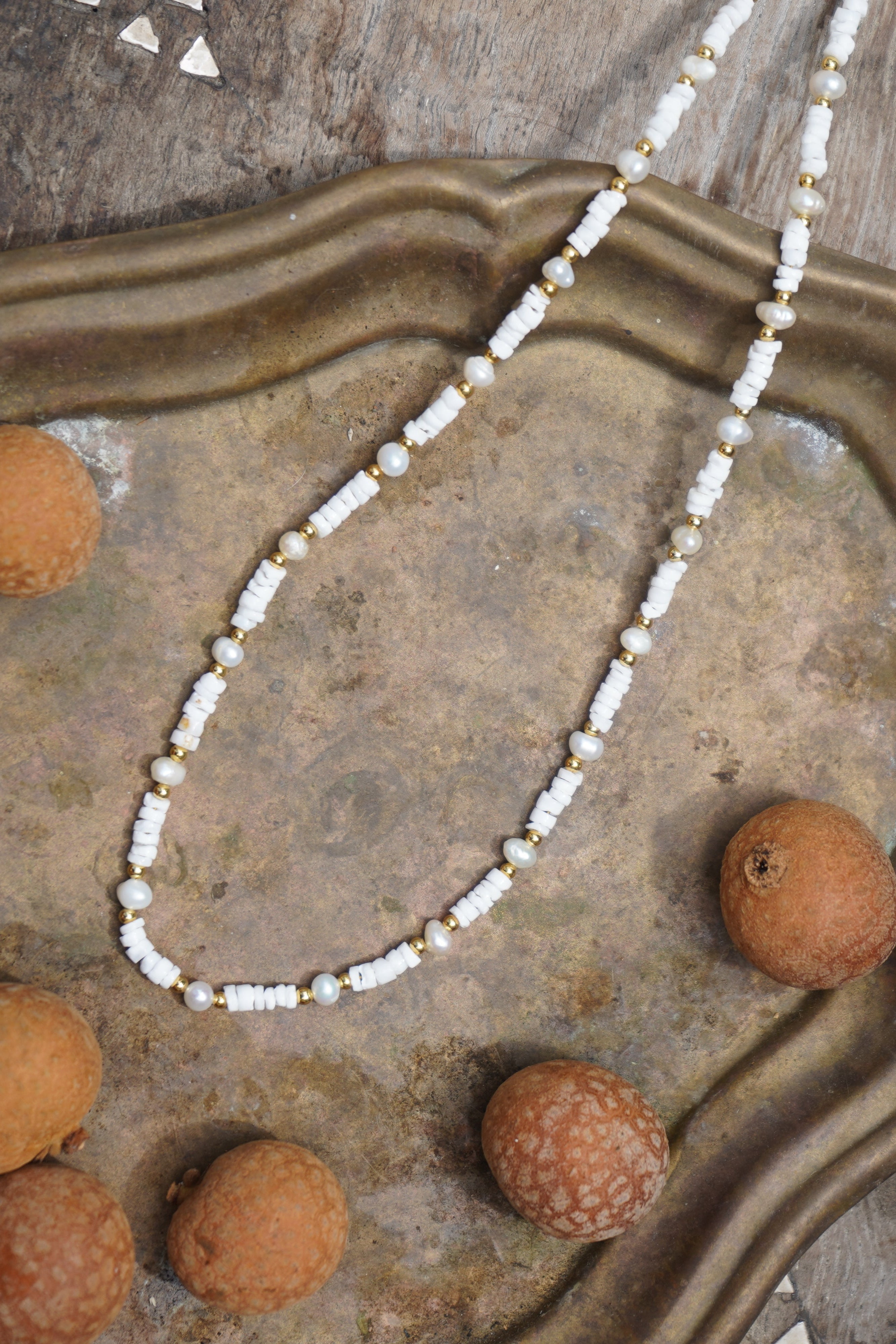 Layer your look with this beachy white necklace crafted from natural puka shells, freshwater pearls, and gold beads. A perfect summer accessory that combines coastal charm with elegant layering potential.

