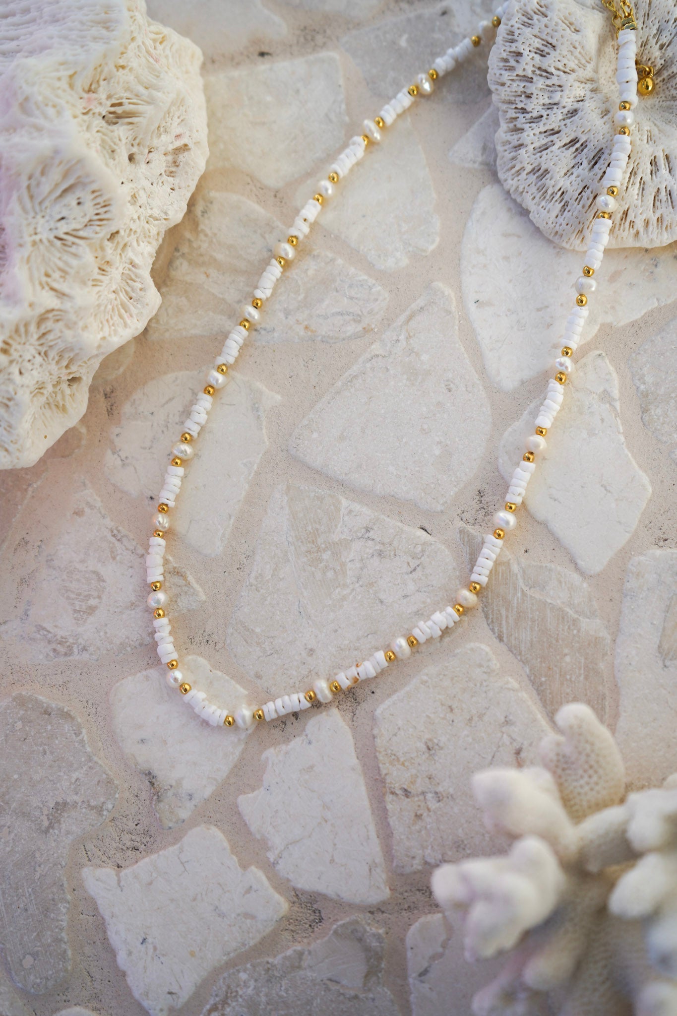 Add a touch of ocean-inspired elegance with our white beaded necklace featuring puka shells, freshwater pearls, and gold accents. Lightweight and versatile, ideal for layering with your favourite jewellery pieces.