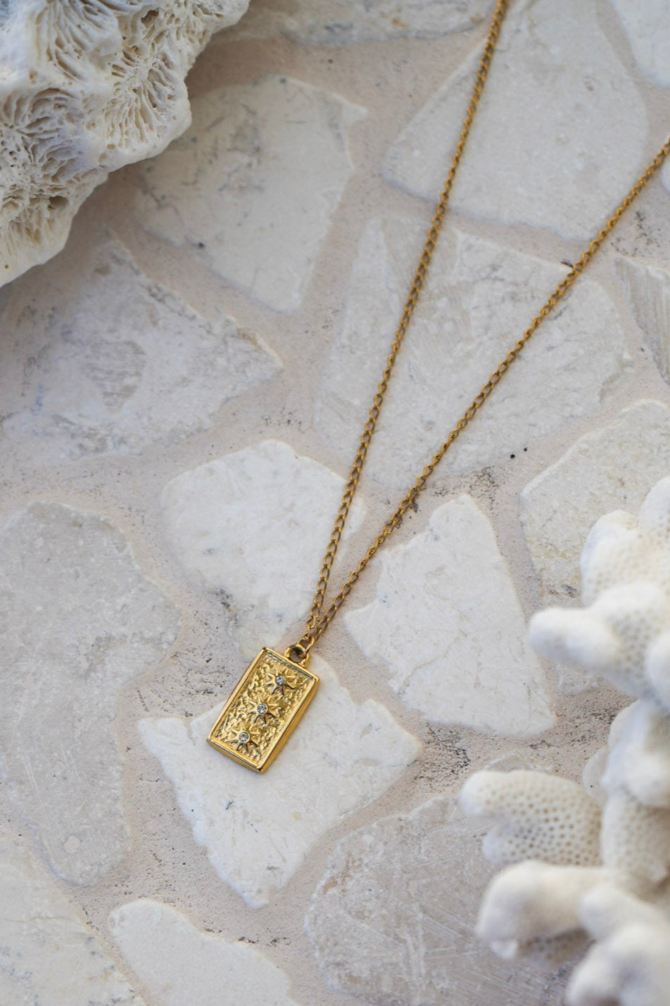 Elevate your jewellery collection with the Junie Necklace, showcasing a gold chain and a rectangle pendant with three suns and center gemstones. Durable, waterproof, and ideal for daily wear.