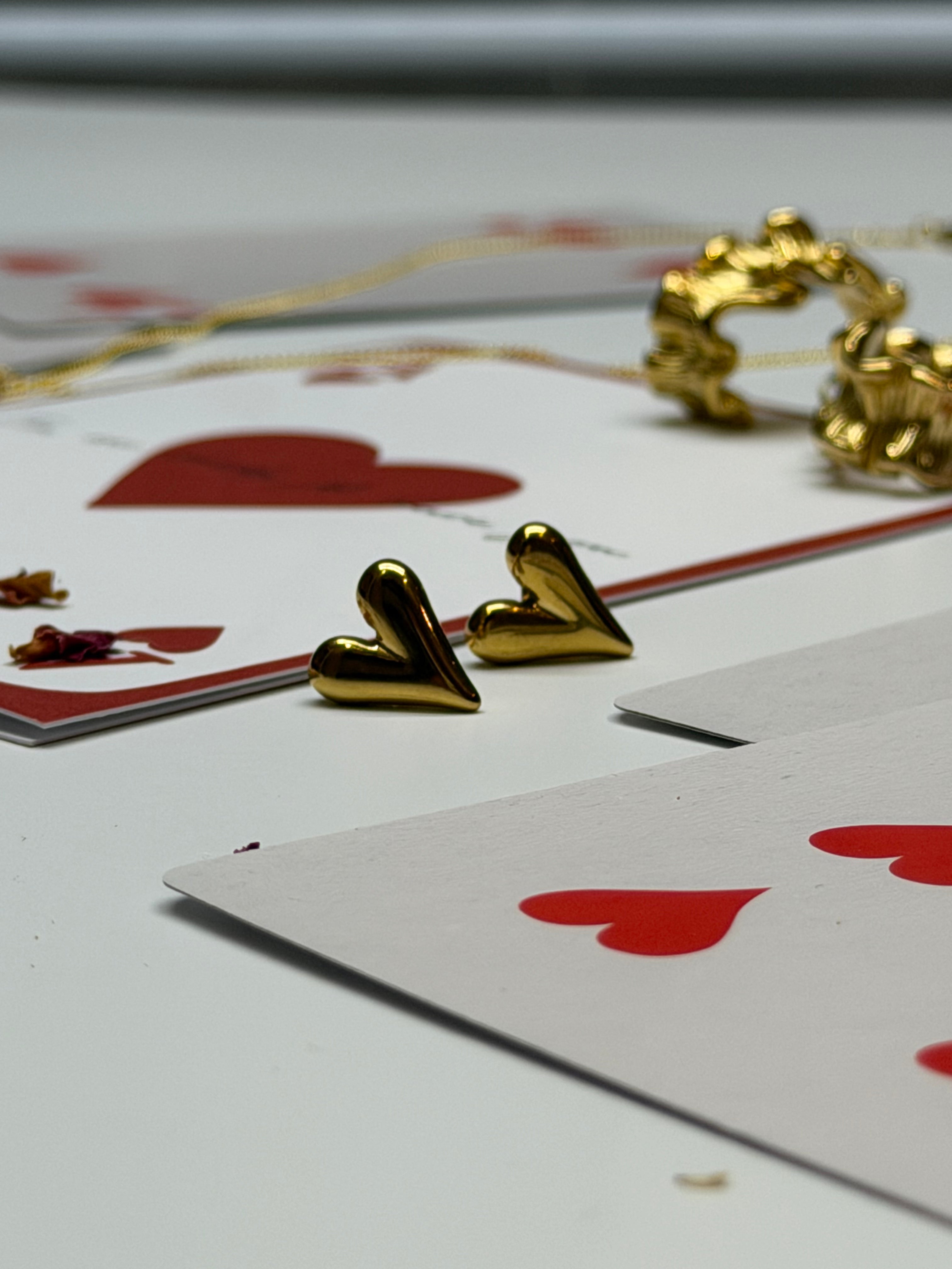 Gold heart-shaped earrings on a playing card with red hearts