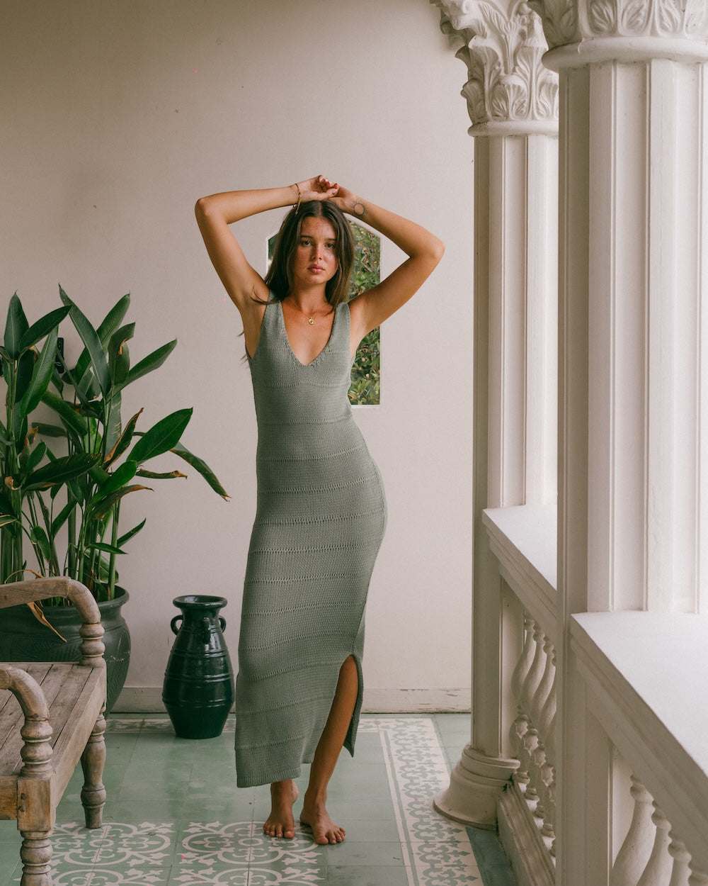 Sage Noa Knit Dress by Malia the Label, sustainably made ribbed knit maxi dress styled in a relaxed pose on an open-air balcony