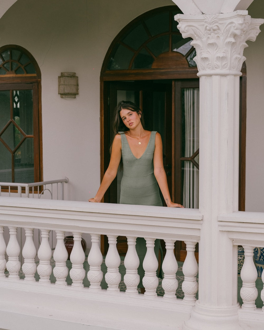 Noa Knit Dress in Sage, ribbed knit maxi dress, model leaning on a white balcony railing in front of an arched wooden doorway