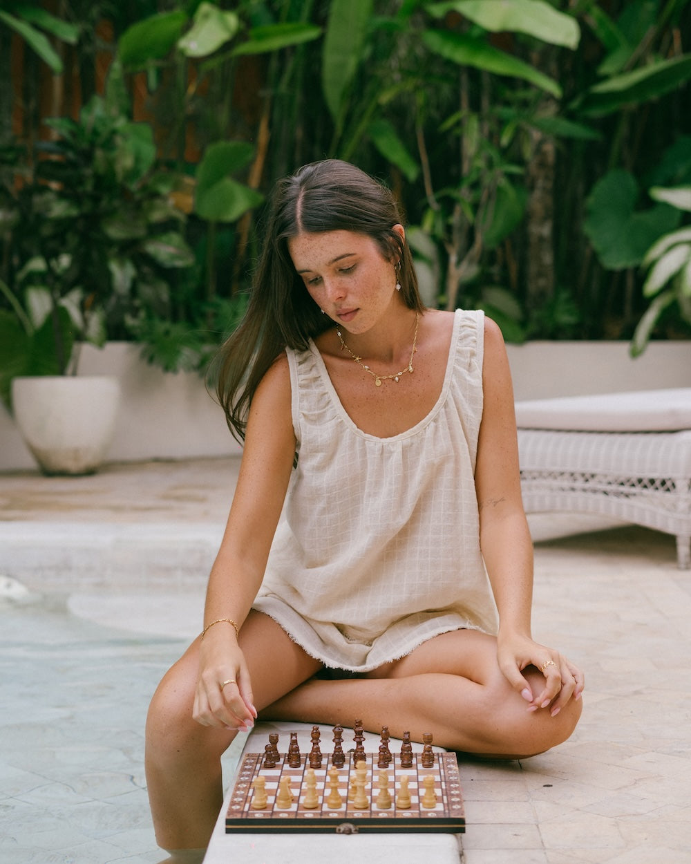Sofia Singlet Top in textured check ramie — model seated cross-legged poolside with chess board, close crop showing gathered rounded neckline and relaxed silhouette — natural fibre singlet top Australia — Malia The Label slow fashion