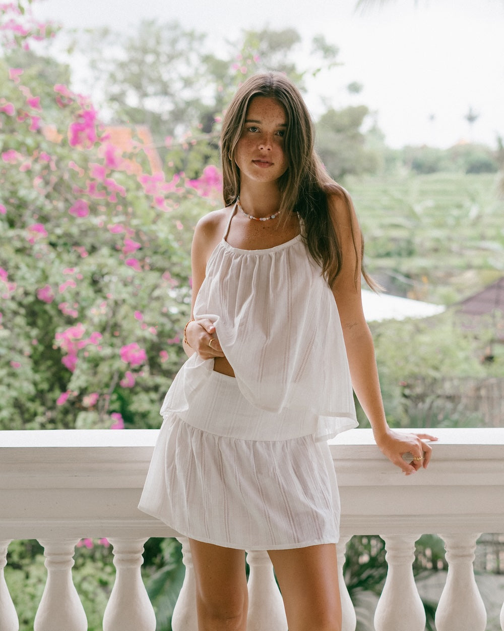Sole Mare Singlet Top and Mini Skirt matching set — full-length front view on villa balcony with bougainvillea backdrop, gathered white halter top and tiered mini skirt showing intricate handloomed cotton detail — white cotton co-ord mini set — Malia The Label La Dolce Vita slow fashion