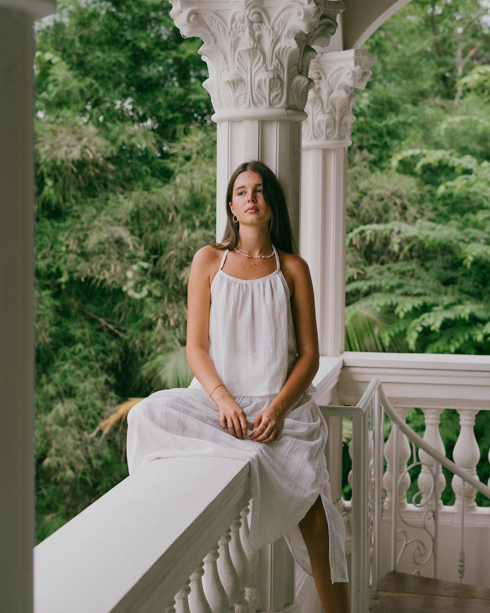 Sole Mare Singlet Top and Maxi Skirt — model seated on ornate white balcony railing, three-quarter front view showing gathered halter neckline and maxi skirt drape in white handloomed cotton — 100% cotton slow fashion matching set — Malia The Label La Dolce Vita collection