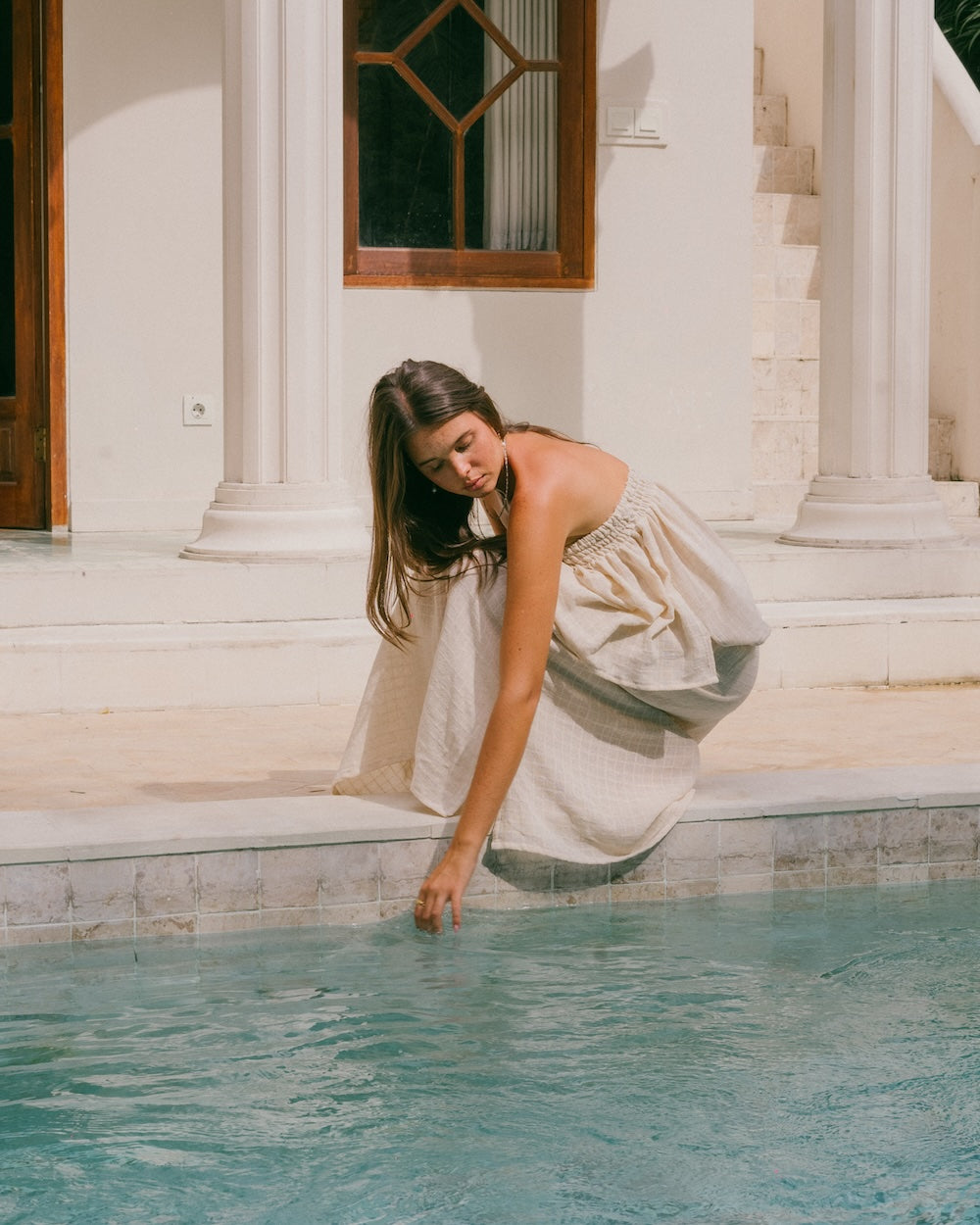 Sorrento top and maxi skirt - model crouches poolside and garment drapes with her detailing gathers and ruffles in natural fibre fabric - Malia the label