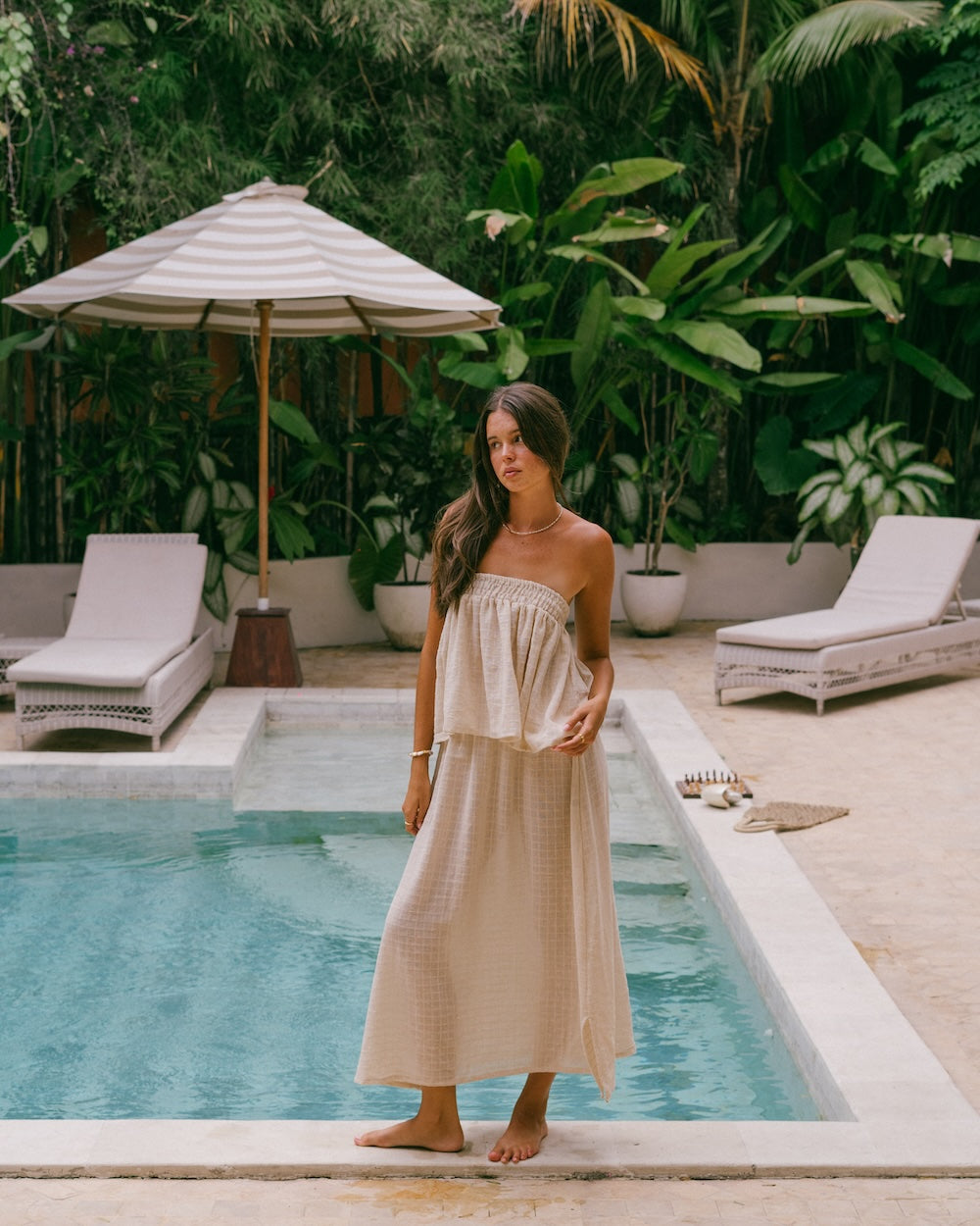 Sorrento Strapless Top and Maxi Skirt complete co-ord set — full-length front view poolside with striped umbrella and tropical garden, shirred bandeau top and floor-length maxi skirt in natural check ramie, barefoot styling — slow fashion ramie matching set Australia — Malia The Label La Dolce Vita