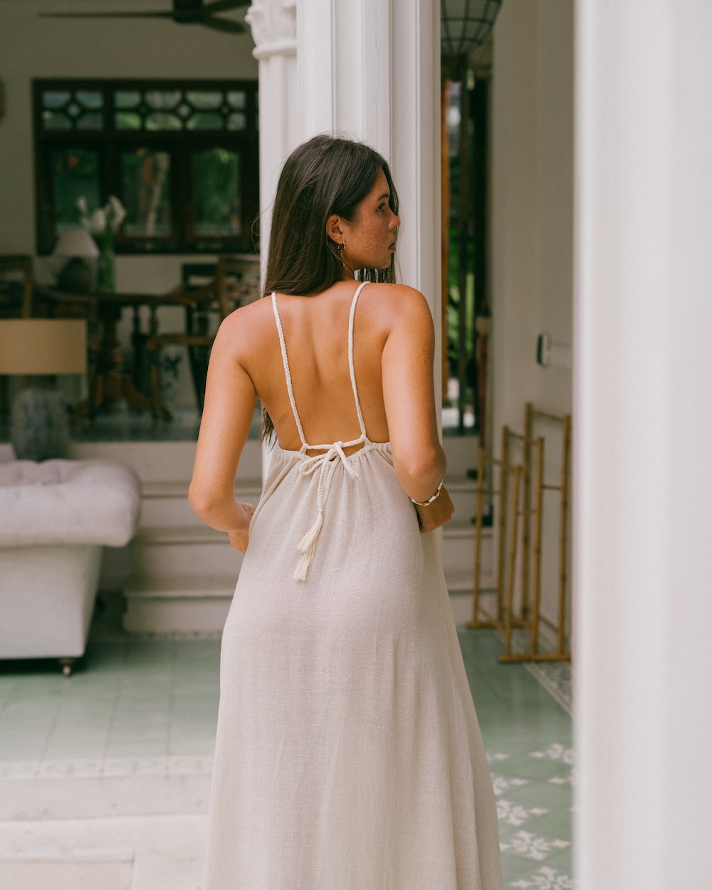Vela Maxi Dress worn in straight-back tie style — rear view showing braided straps running from shoulders to low back tied in a knot with tassel detail — convertible open back natural ramie maxi dress — Malia The Label La Dolce Vita slow fashion